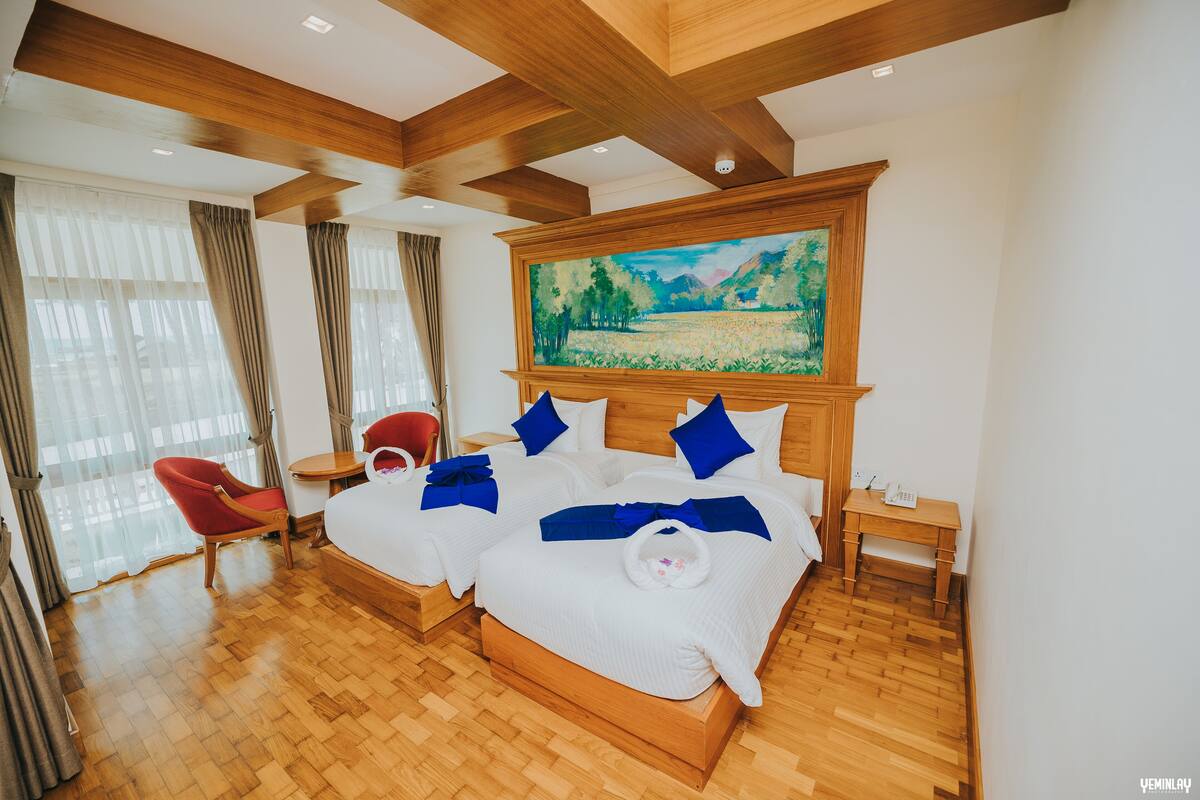 A hotel room with a large bed, two bedside tables, a red chair, a small table, and a painting on the wall.