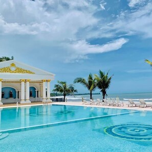 Un área de piscina con sillones de descanso, palmeras y un edificio con columnas.