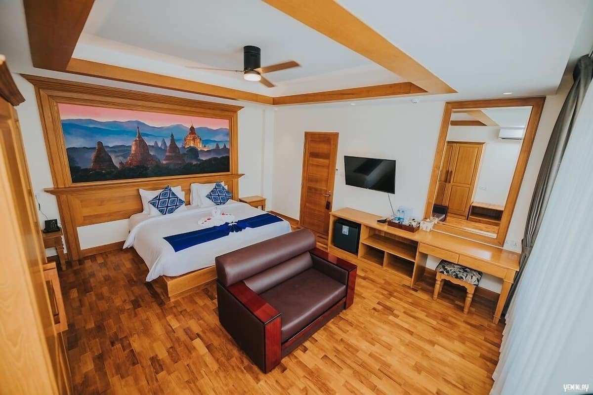 A bedroom with a bed, a sofa, a TV, and a painting of a landscape.
