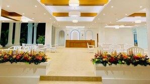 Un área de recepción con un mostrador central, sillas blancas y arreglos florales.