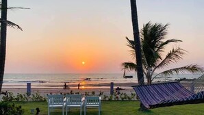 Escena de playa con una hamaca, dos sillas blancas y palmeras.