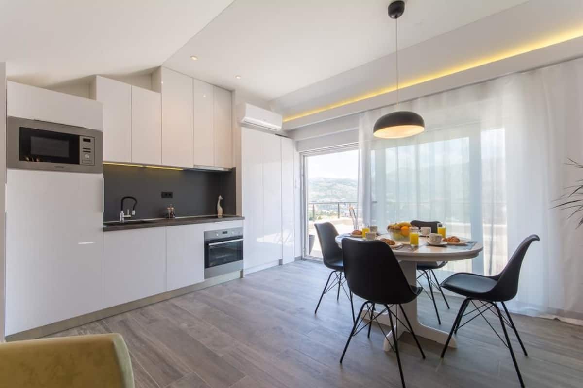 Une cuisine moderne avec des meubles blancs, un four à micro-ondes encastré et un coin repas comprenant une table ronde et des chaises noires.
