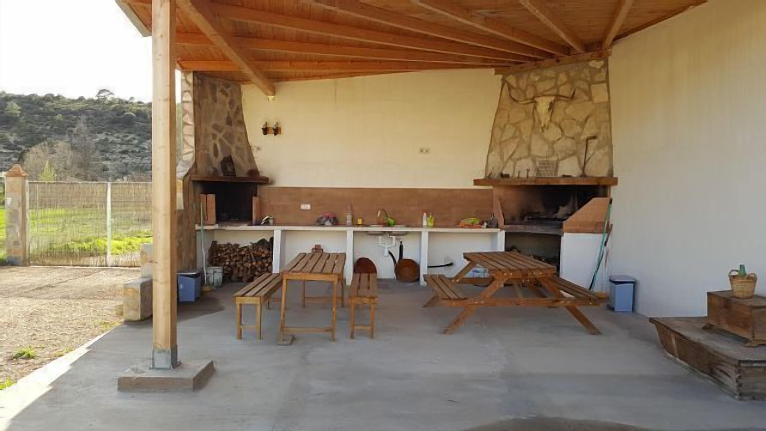 Une terrasse extérieure dotée d’une cheminée en pierre, de tables en bois et d’un espace barbecue.