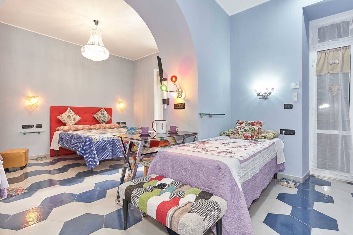 A hotel room with two beds, a dining table, a bench, and a chandelier.