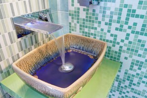 A square ceramic sink with a blue basin, a faucet, and a green and white tiled wall.