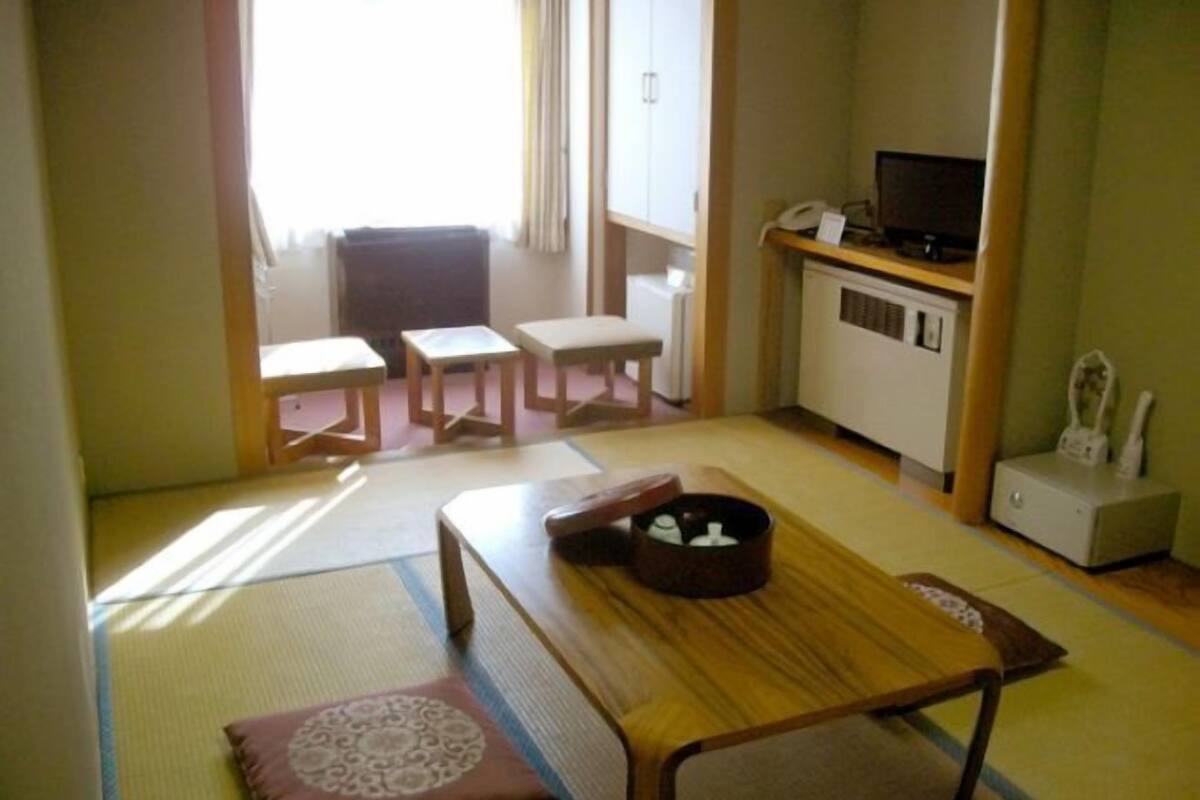 Een traditionele Japanse kamer met tatami vloerbedekking, een lage houten tafel, een kussenbank en een kleine televisie op een kast.
