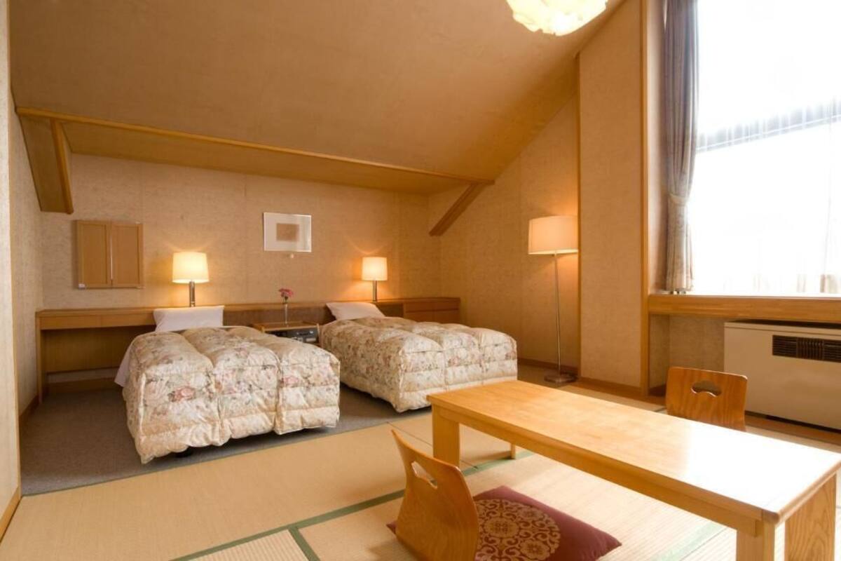 Een kleine, knusse kamer met twee bedden, een houten tafel en een raam met gordijnen.