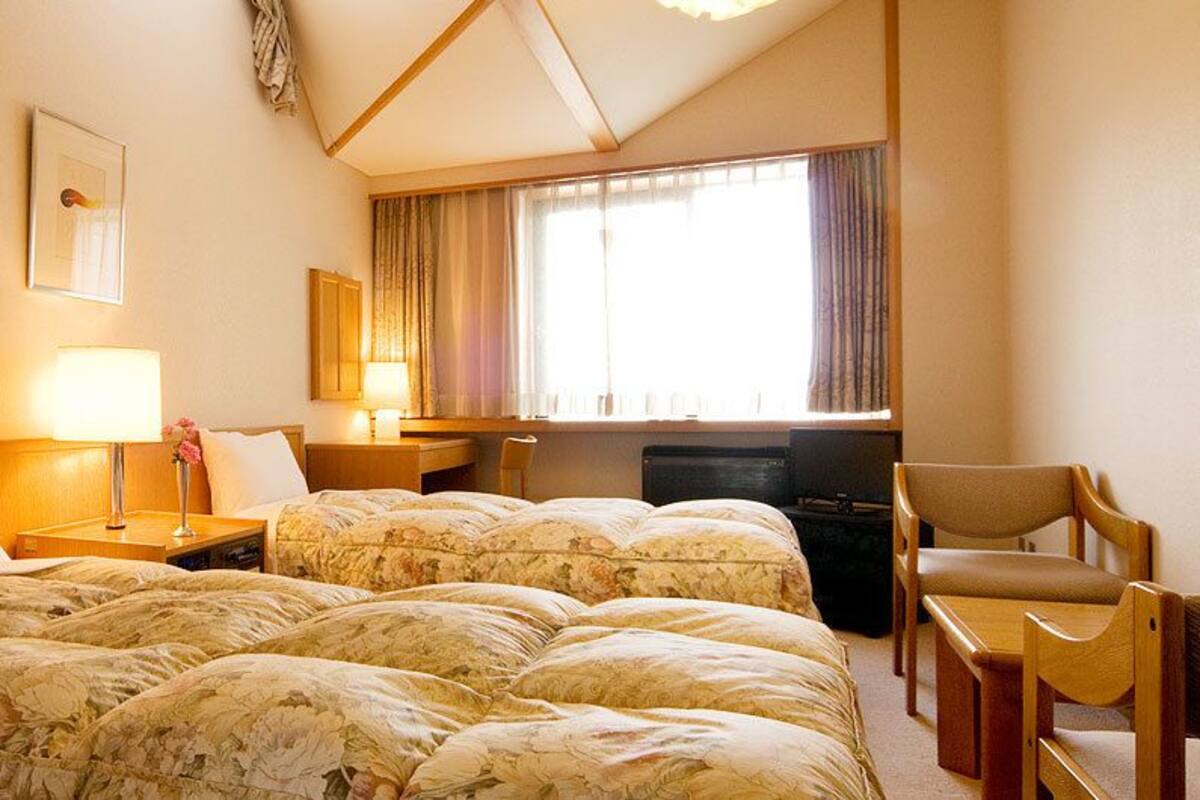 Een hotelkamer met twee bedden, een bureau, een stoel, een televisie en een raam met gordijnen.