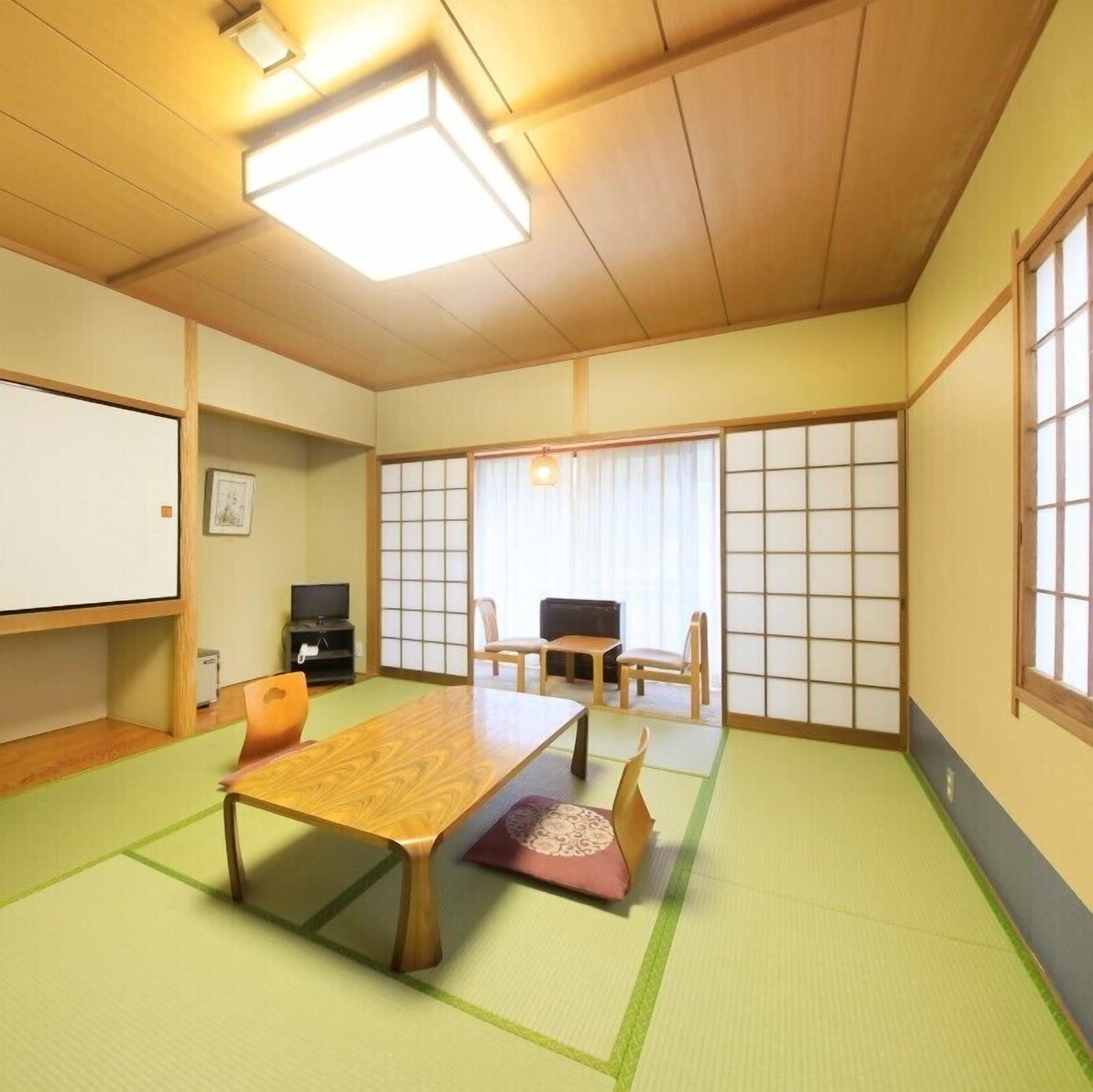Una habitación tradicional japonesa con suelo de tatami, una mesa de madera baja y puertas correderas.