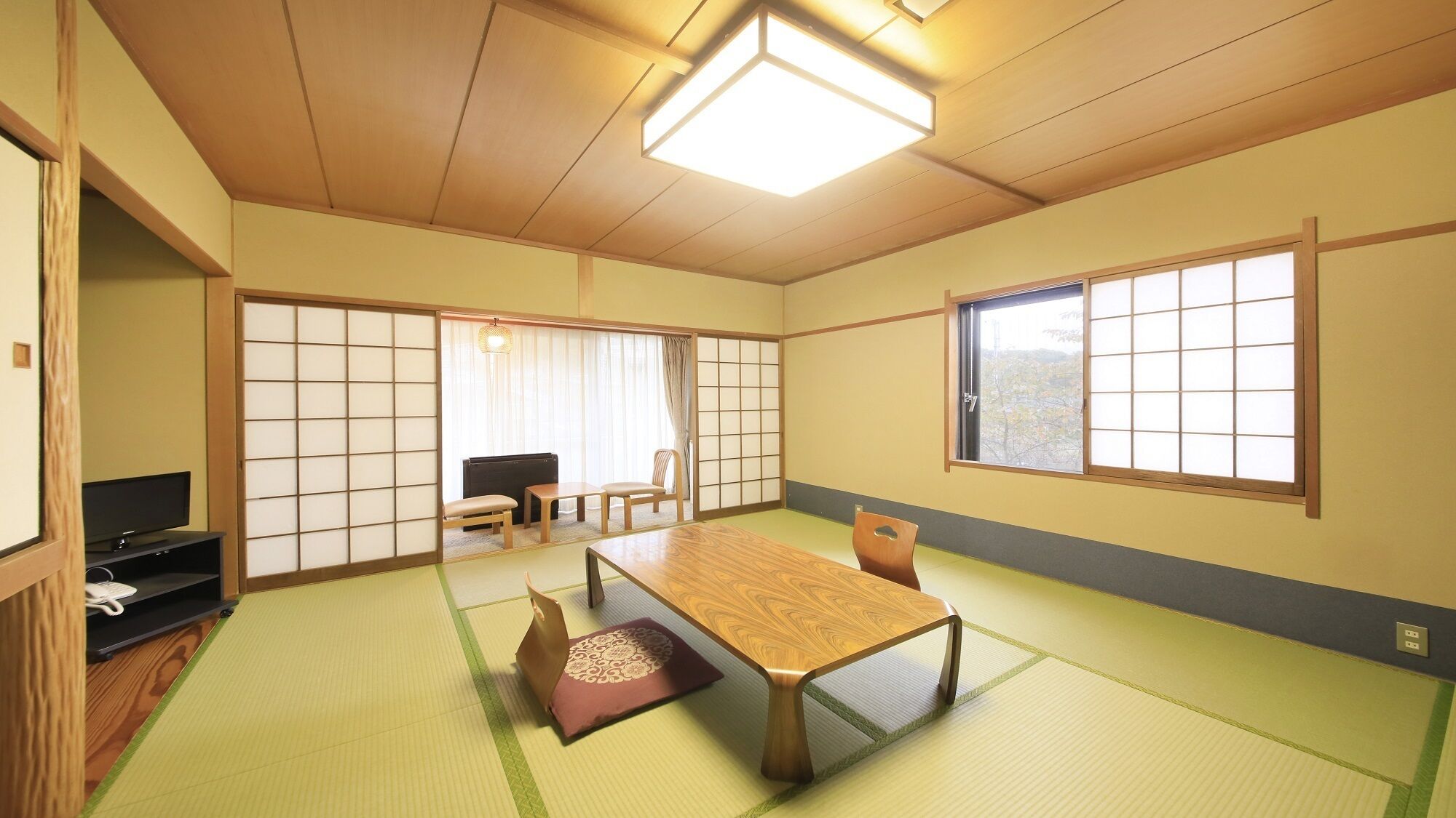 Una habitación tradicional japonesa con suelo de tatami, una mesa baja, un televisor y puertas correderas.