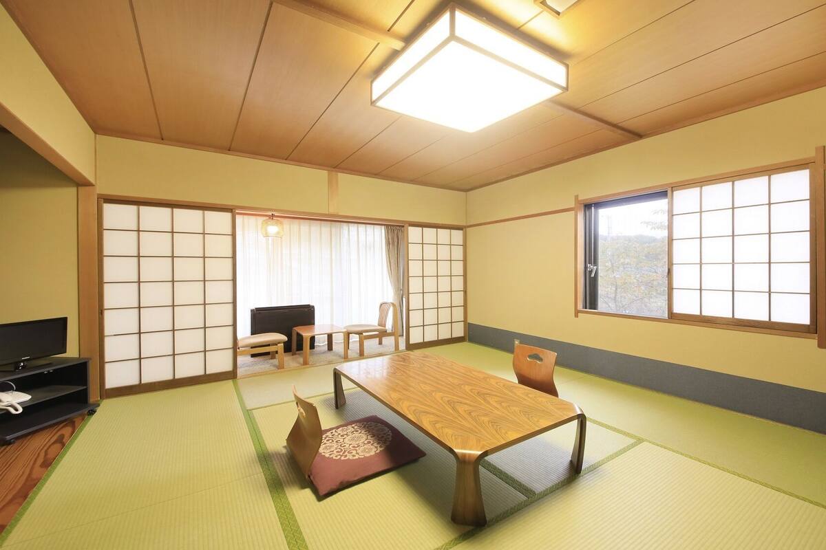 Een traditionele Japanse kamer met tatami vloerbedekking, een lage tafel, een televisie en schuifdeuren.