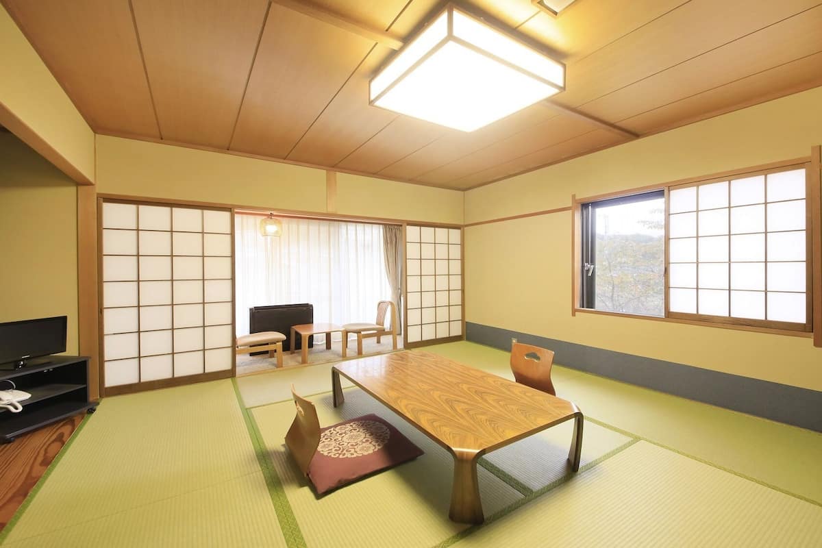 Una habitación tradicional japonesa con suelo de tatami, una mesa baja, un televisor y puertas correderas.