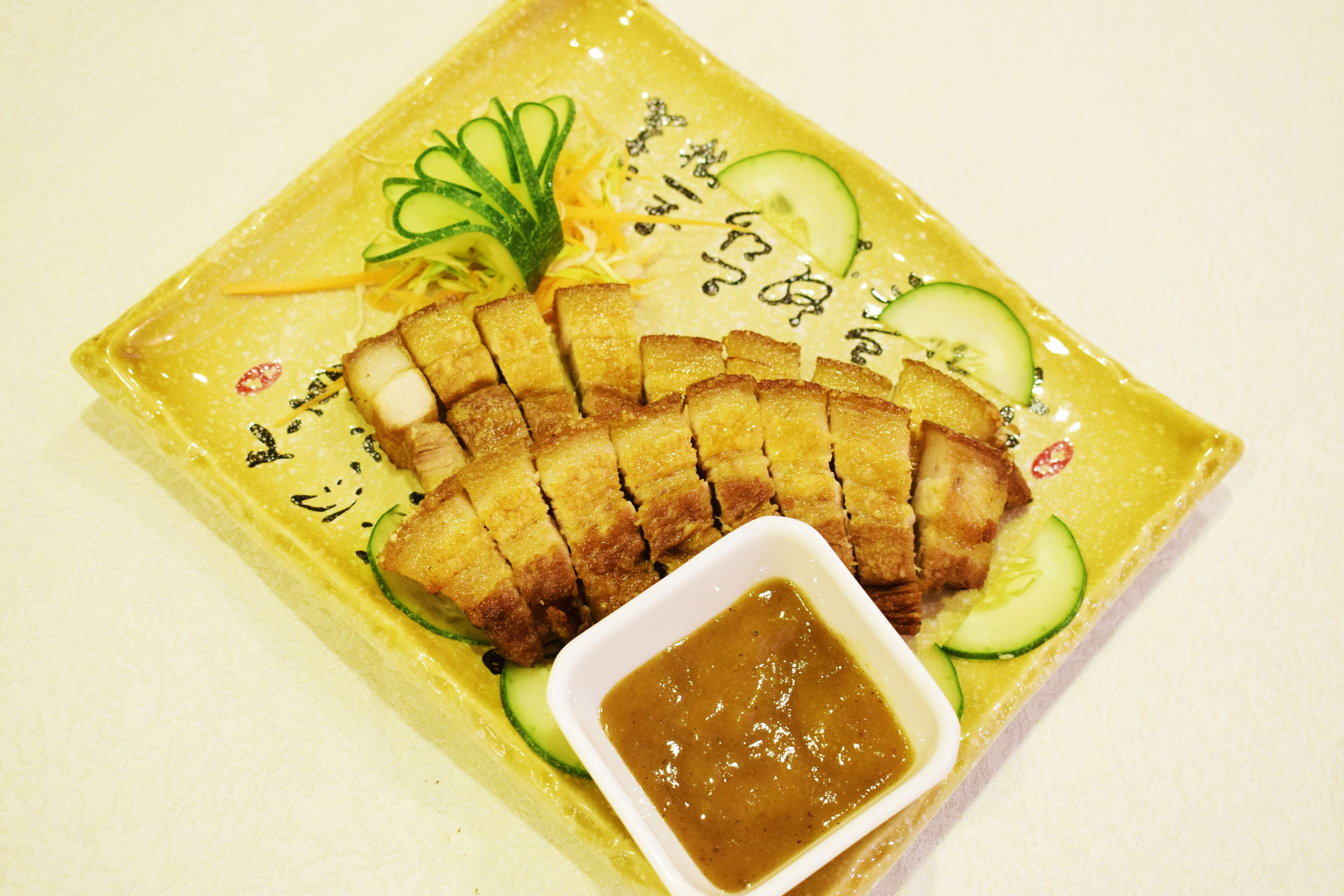 Un plato de carne en rodajas con rodajas de pepino y un recipiente pequeño de salsa.