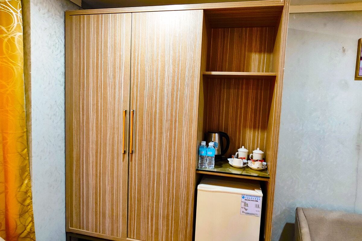 Ein Zimmer mit einem Holzschrank, einem kleinen Kühlschrank und einem Regal mit Wasserflaschen und Teekannen.