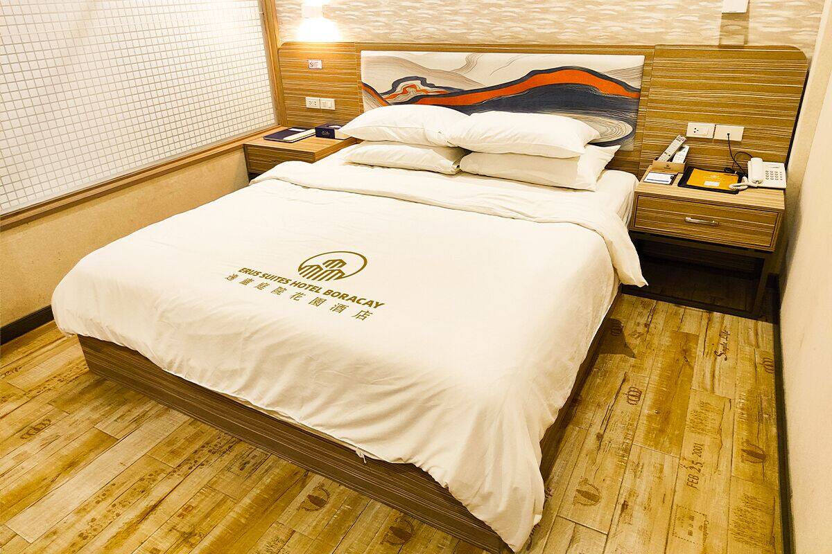 Une chambre d’hôtel avec un lit, une tête de lit en bois, des tables de chevet et une petite table de nuit avec un téléphone et une lampe.