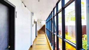 A corridor with a wooden floor, large windows, and a staircase leading to an outdoor area with plants. -  ERUS SUITES HOTEL BORACAY (Boracay Island)