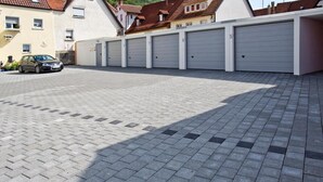 A parking area with six garage doors, a paved surface, and a car parked in the foreground. - Hotel Buck (Bad Urach)