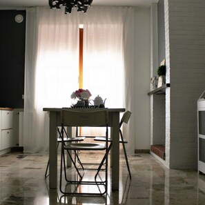Een eetruimte met een tafel en stoelen, een vaas met bloemen en een raam met gordijnen.