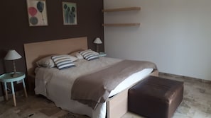 Een slaapkamer met een bed, kussens, een nachtkastje met een lamp, een nachtkastje met een lamp, en een muur met twee schilderijen.
