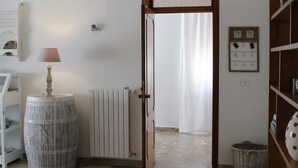 A hallway with a white radiator, a lamp, a round barrel, a wicker basket, and a wooden bookshelf. - B&Be Home (Tollo)