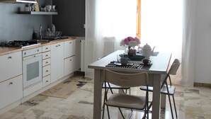 A kitchen with a stove, oven, and cabinets, a dining table with chairs, and a window with curtains. - B&Be Home (Tollo)