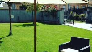A well-maintained grassy patio area with outdoor furniture, including a chair and a small table, and a decorative umbrella providing shade. - B&Be Home (Tollo)