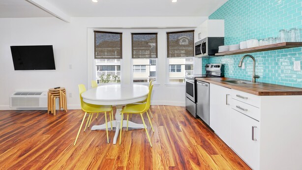A modern kitchen with a white dining table, yellow chairs, and a blue-tiled backsplash.