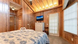 A wooden-paneled bedroom with a bed, dresser, and a television.