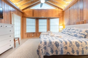 A room with a wooden ceiling, a bed with a blue and white patterned bedspread, a dresser, and a window with blinds. - Pet-Friendly Beach Cottage on St. Simons Island | Walk to Beach & Pier Village (St Simons)