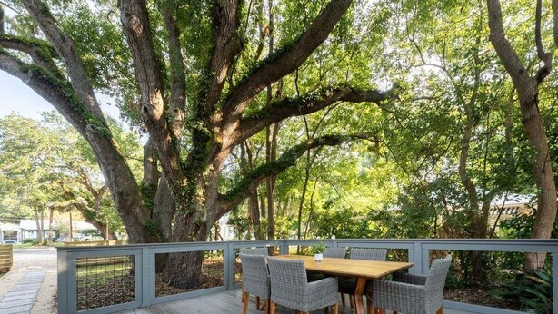 An outdoor deck with a wooden table and wicker chairs, surrounded by large trees.