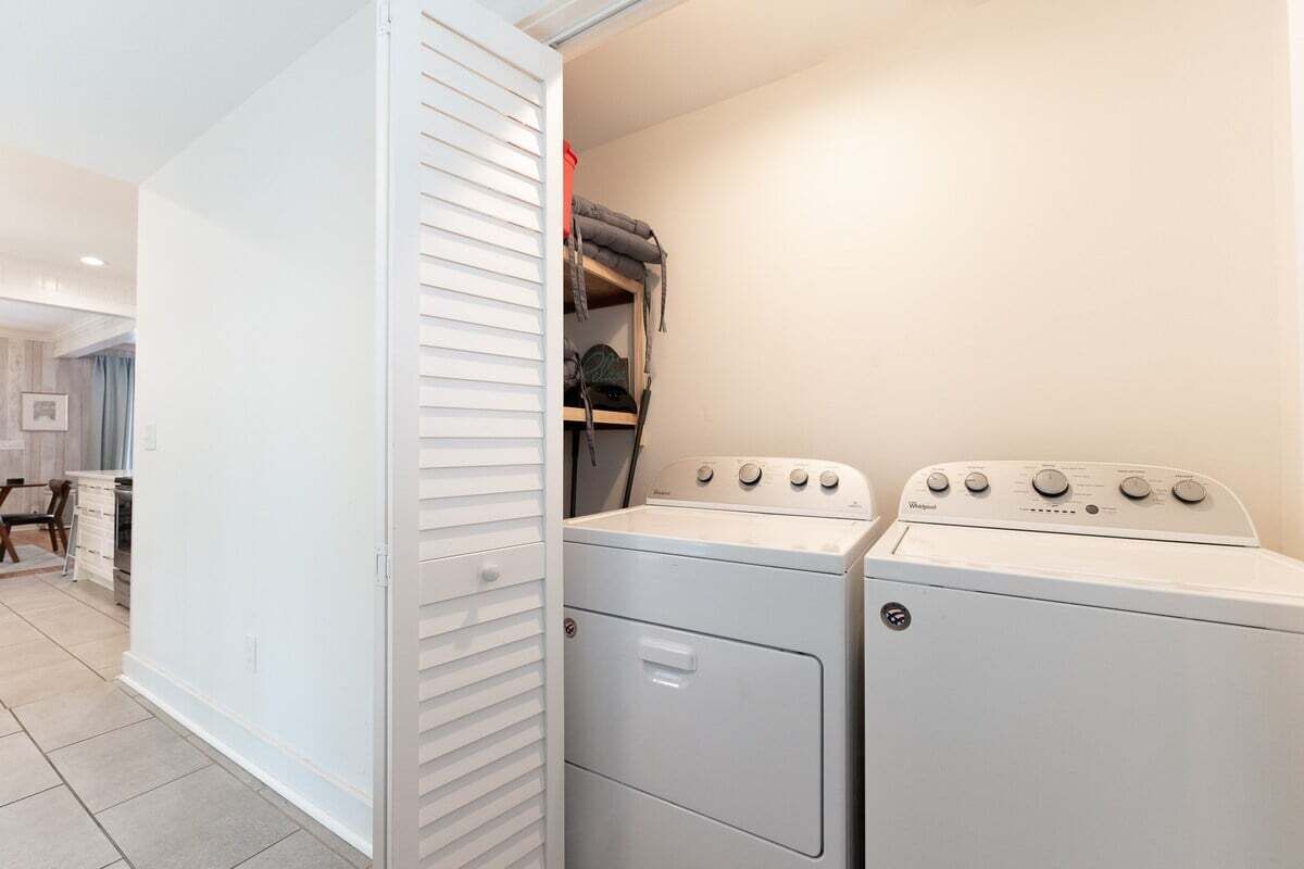 A laundry room with a stacked washer and dryer, a white wall, and a door with louvered blinds.