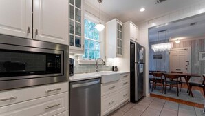 A modern kitchen with white cabinetry, stainless steel appliances, and a dining area with wooden furniture.