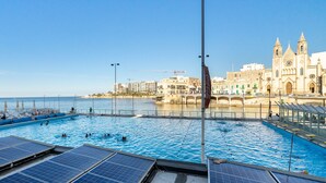 A swimming pool with solar panels, a waterfront view, and a historic building in the background.