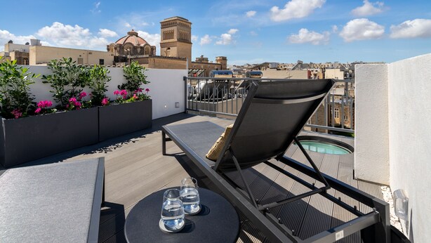 A rooftop terrace with a lounge chair, a table with glasses, and a view of the cityscape and a historic building.