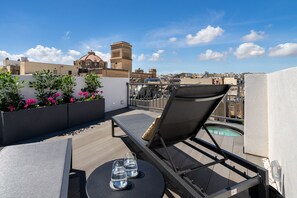 Terraza en la azotea con una silla de descanso, una mesa con vasos y vistas del paisaje urbano y un edificio histórico.