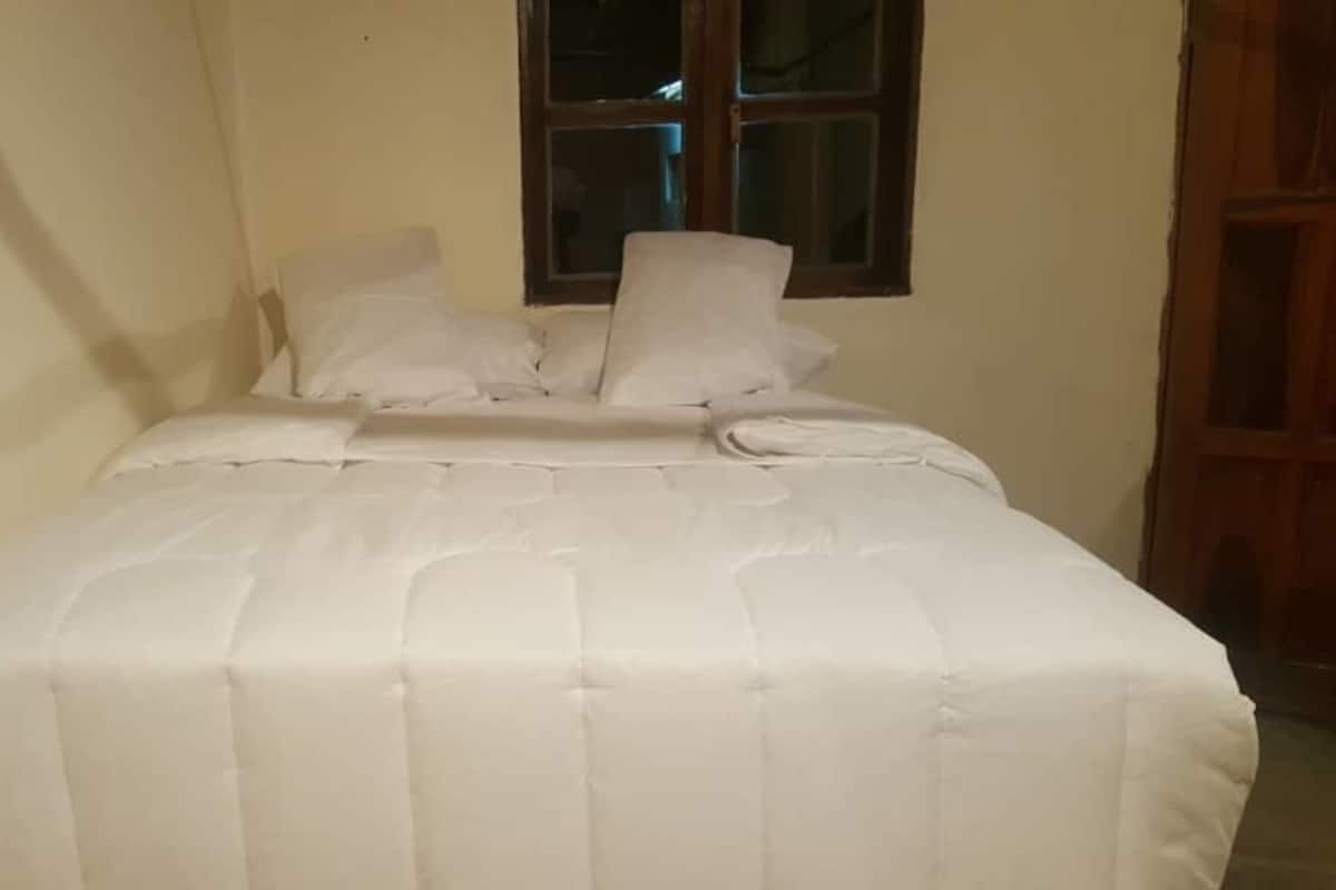 A neatly made bed with a white bedspread and pillows in a room with a window and a wooden door.