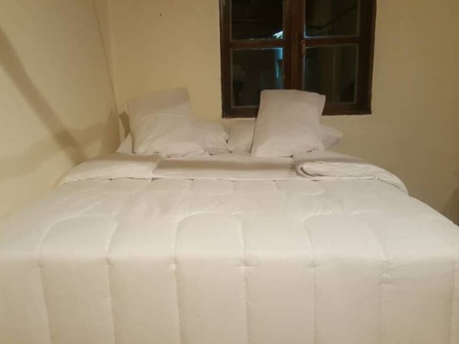 Una cama bien hecha con cubrecama y almohadas blancas en una habitación con ventana y puerta de madera.