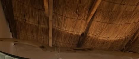 A bed with a canopy in a room with a thatched roof.