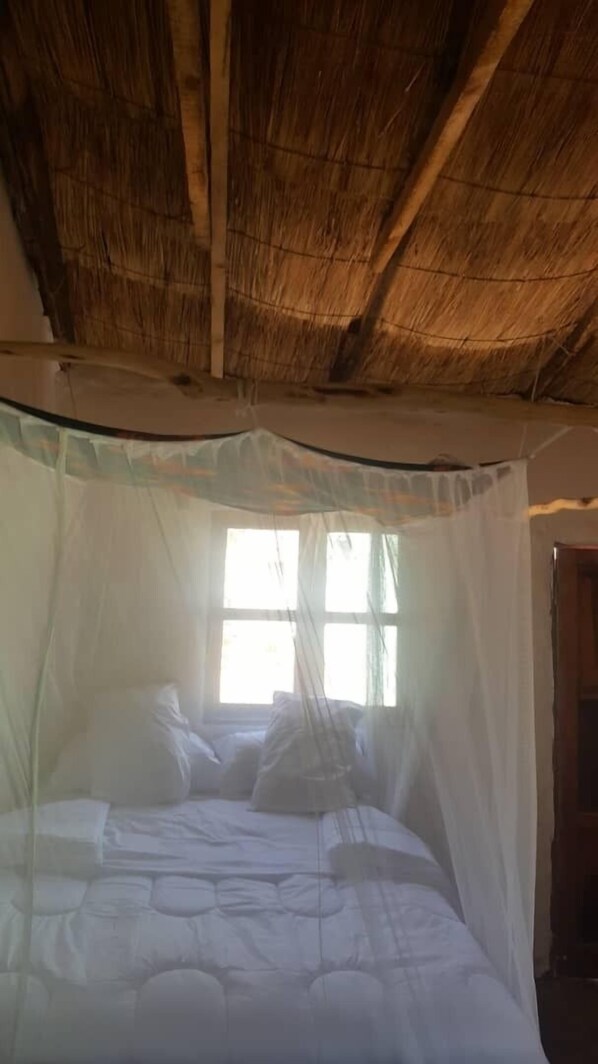 A bed with a canopy in a room with a thatched roof.