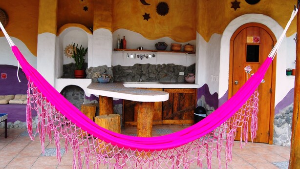 A cozy outdoor seating area with a wooden table and chairs, a hammock, and a rustic stone wall with decorative elements. - House Dalia. Beautiful, cozy and independent house. Quiet in contact with nature (Tumbaco)