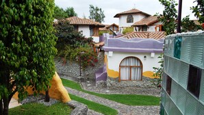 A courtyard with a stone pathway, a small tree, and a building with a tiled roof. - House Dalia. Beautiful, cozy and independent house. Quiet in contact with nature (Tumbaco)