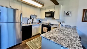 A modern kitchen with white cabinets, stainless steel appliances, a granite countertop, and a wooden ceiling beam.