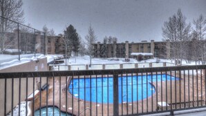 A snow-covered outdoor area with a swimming pool, surrounded by a fence and buildings in the background.