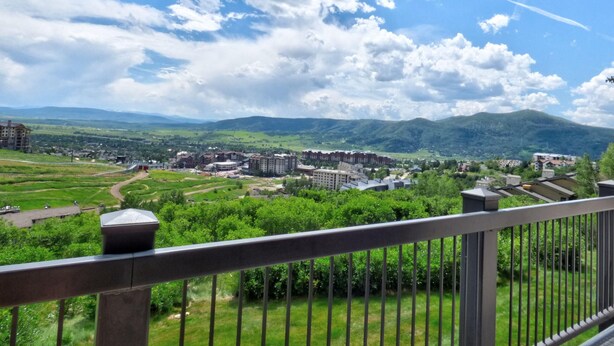 A balcony with a view of a town, green fields, and mountains.