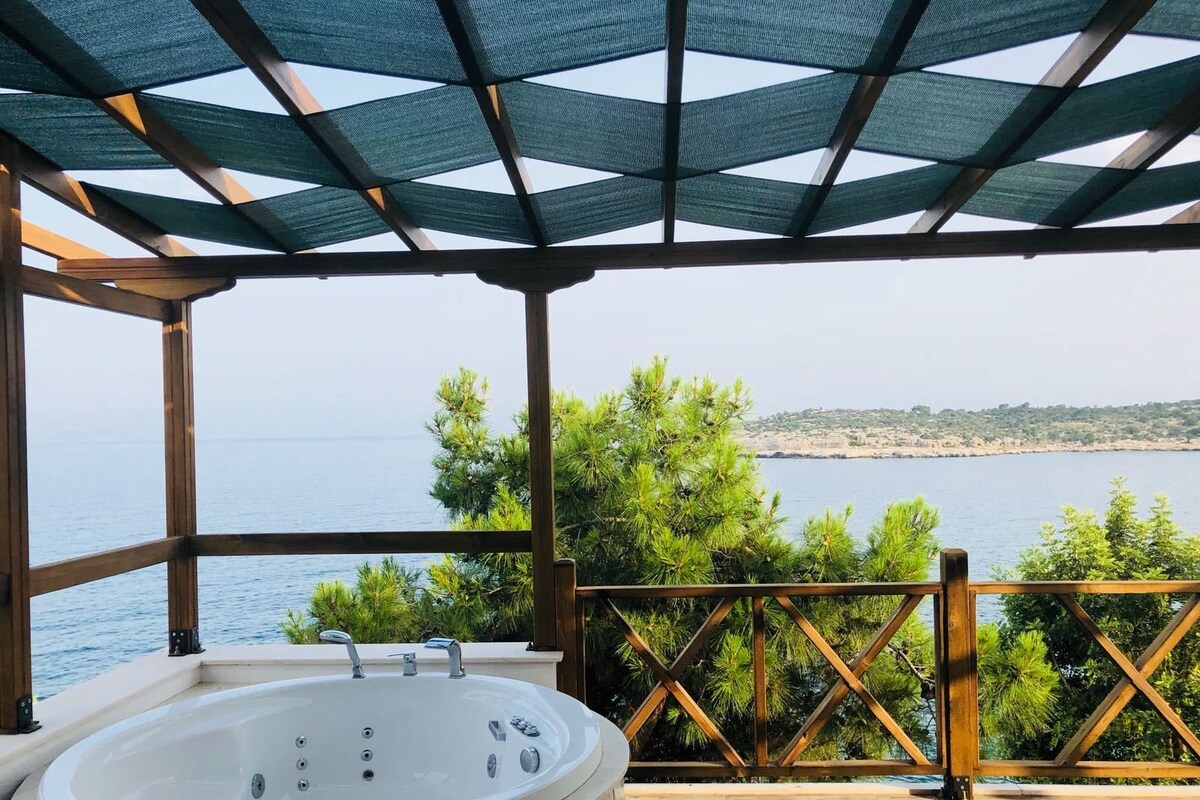 Un bain à remous installé sous une pergola, offrant une vue sur la mer et la verdure.