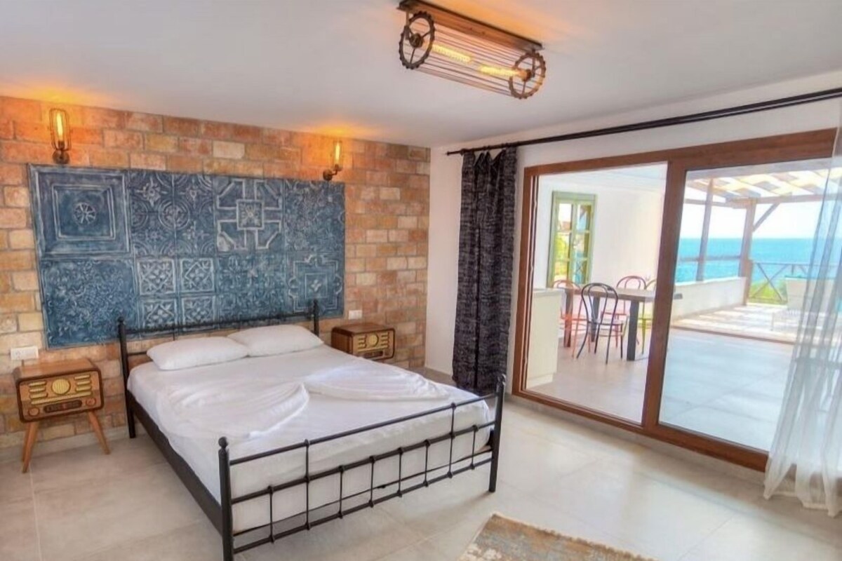Une chambre avec un lit, un mur décoré de carreaux, une radio et une vue sur un espace extérieur comprenant une table et des chaises.