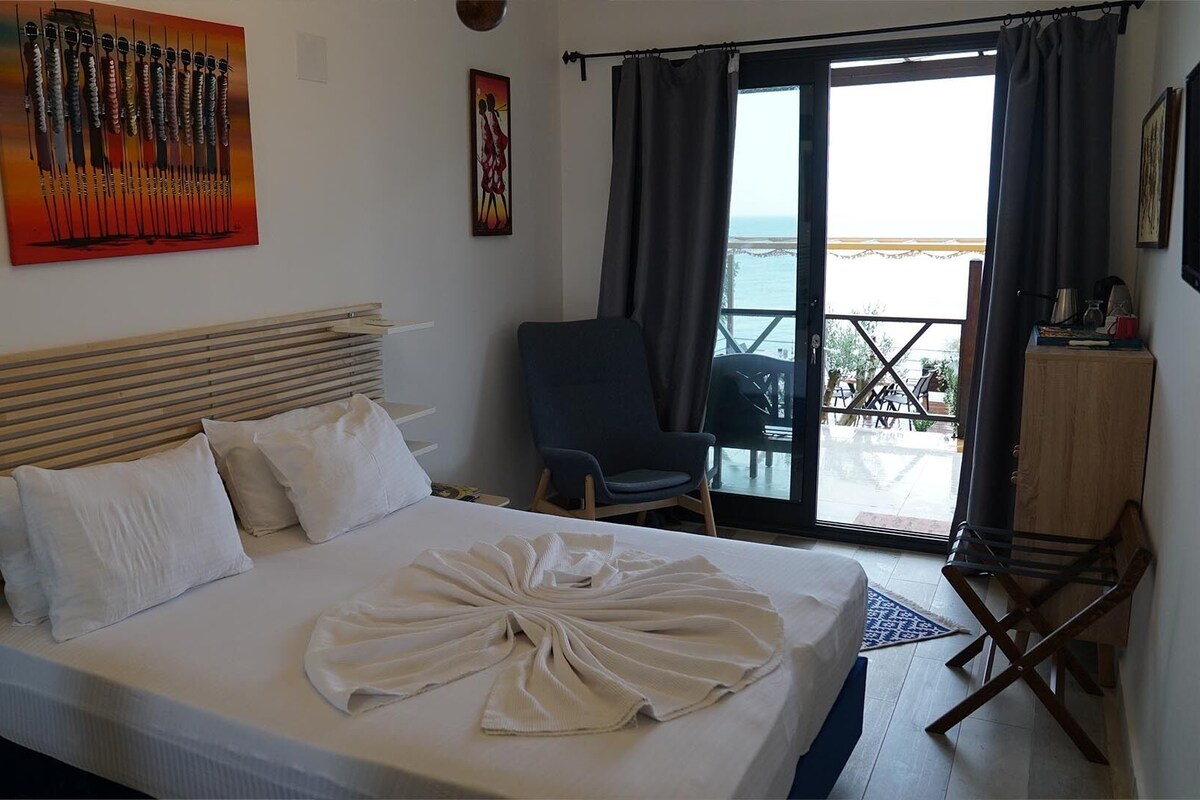 Une chambre d’hôtel avec un lit, une chaise, un bureau et une vue sur la mer par la fenêtre.