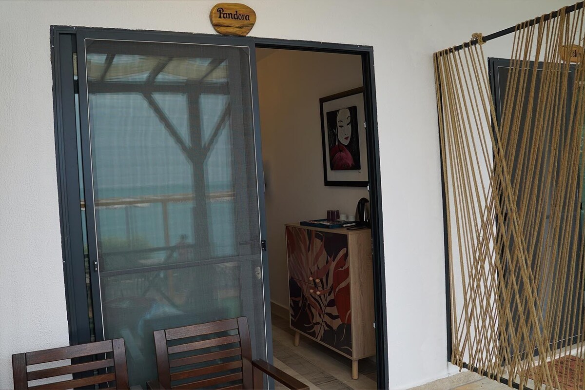 Une pièce dotée d’une porte-fenêtre coulissante donnant sur un balcon, d’une petite table avec des chaises et d’un panneau décoratif orné de motifs floraux.