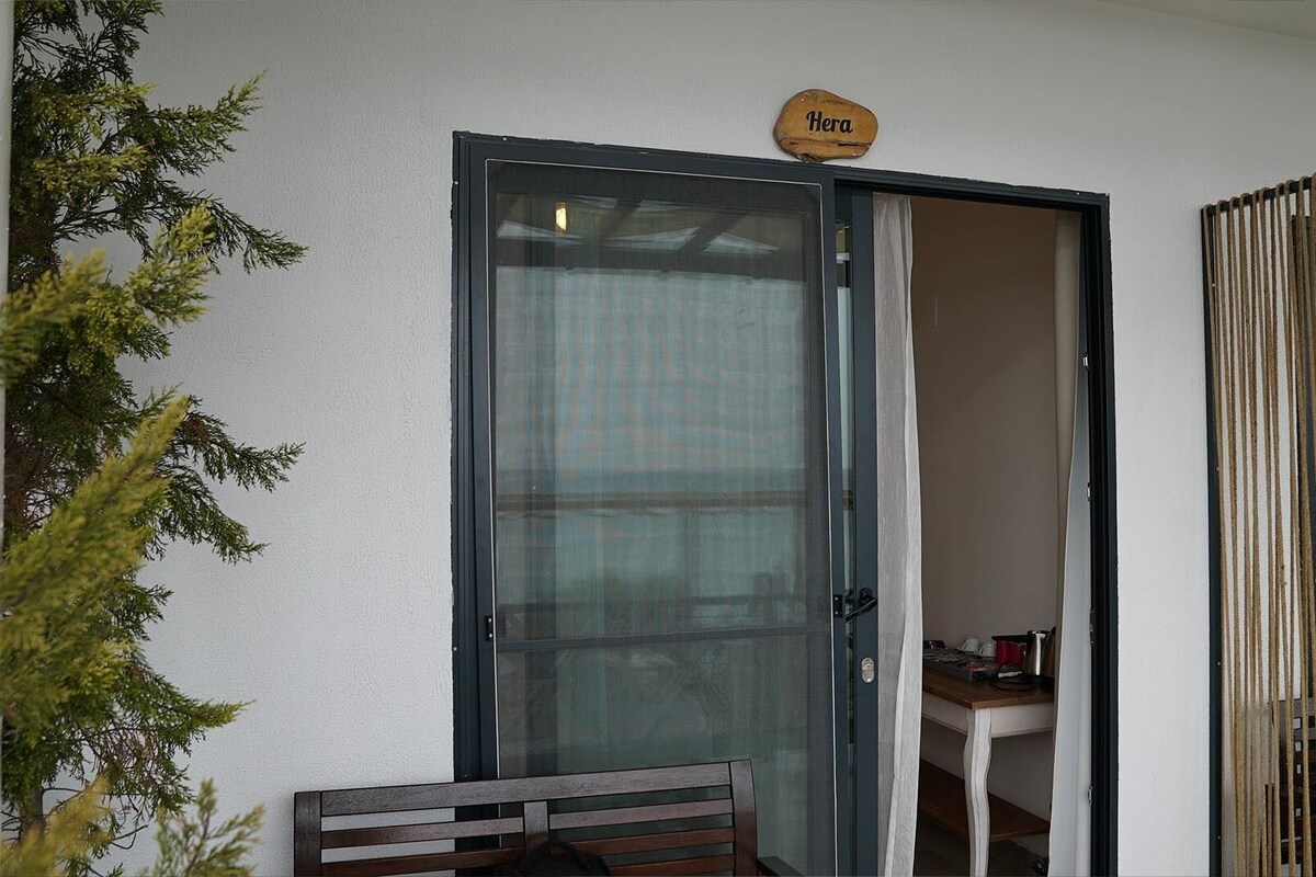 Une pièce dotée d’une porte-fenêtre coulissante, d’un banc en bois, d’une petite table sur laquelle sont posés divers objets, et d’une enseigne au-dessus de la porte portant l’inscription « Herald ».