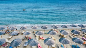 Ein Strand mit Reihen von Liegestühlen und Reetsonnenschirmen, freier Blick auf das Meer und eine entfernte Insel.